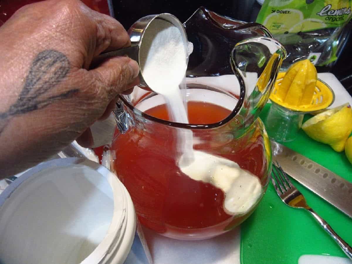 Collagen powder being added to a glass pitcher of pink lemonade.