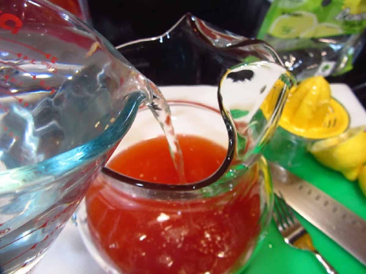 Water being added to a pitcher of pink lemonade.
