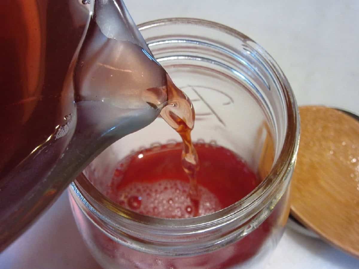 Pouring strawberry simple syrup into a mason jar.
