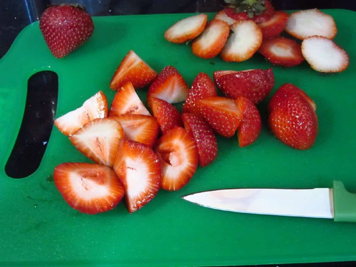 Chopped strawberries on a cutting board with a paring knife.