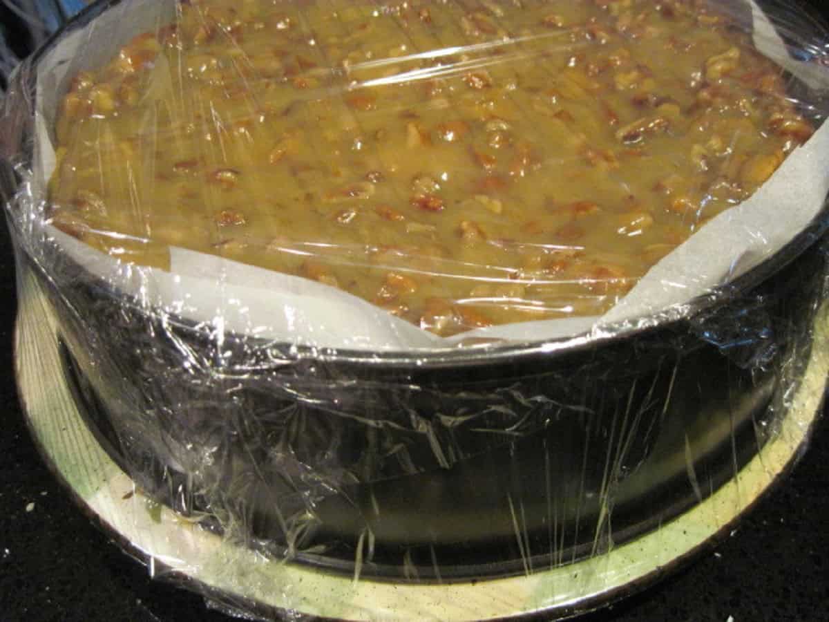 A maple pumpkin cheesecake in a springform pan and covered with parchment paper and plastic wrap.