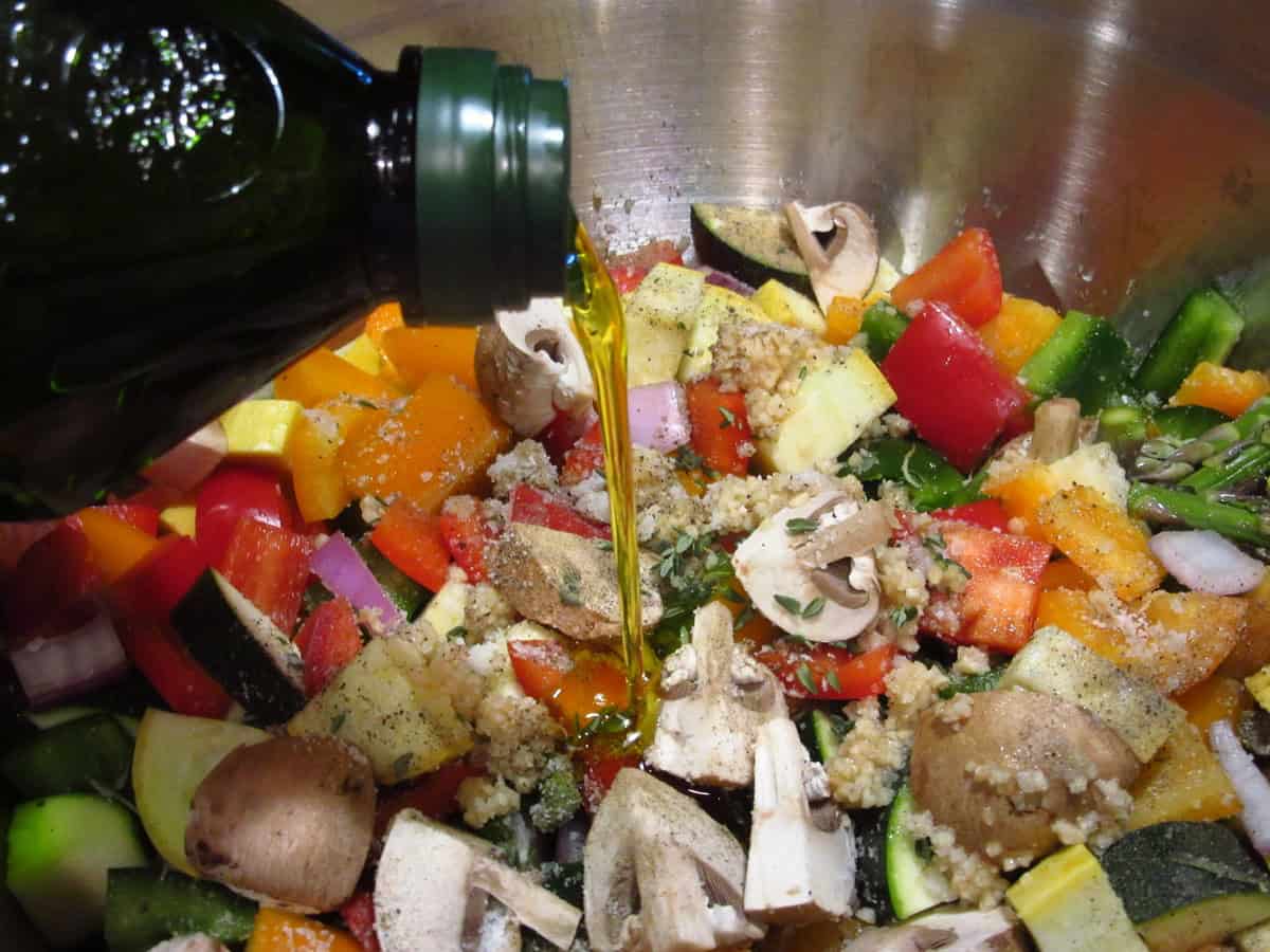Olive oil being poured into colorful rainbow vegetables in a bowl.