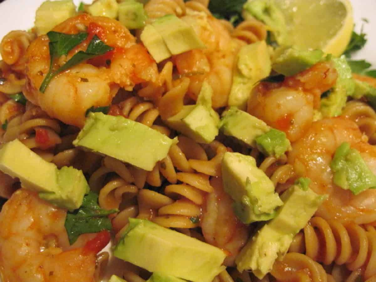 A plateful of cooked rotini pasta, shrimp, and avocado in a spicy sauce.