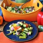 A blue plate filled with roasted rainbow vegetables in the foreground with a casserole dish in the background.