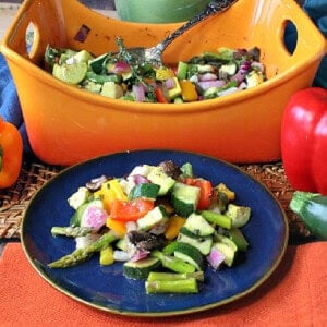 A blue plate filled with roasted rainbow vegetables in the foreground with a casserole dish in the background.