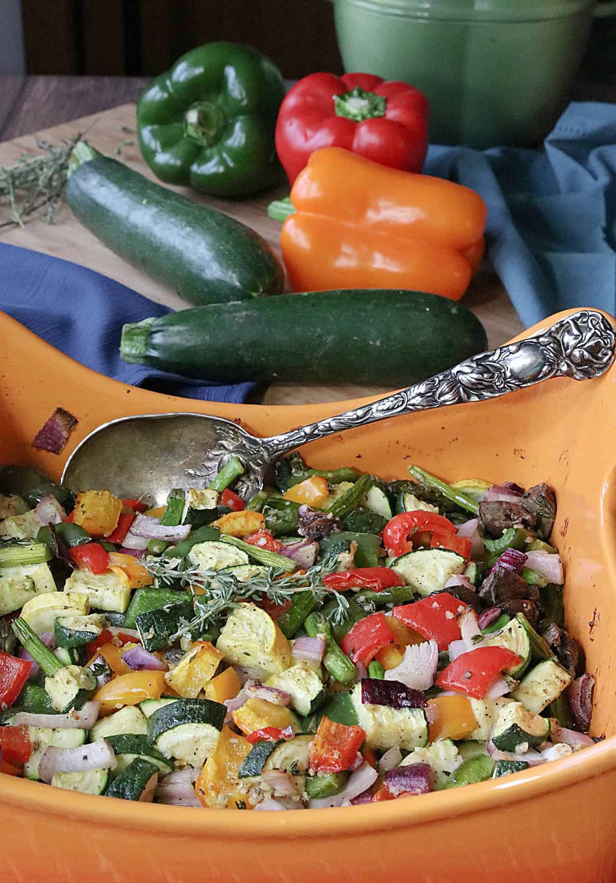 Fresh, whole vegetables in the background with a casserole filled with Summertime's Roasted Rainbow Vegetables.