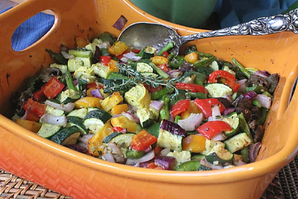 An orange casserole dish filled with Summertime's Roasted Rainbow Vegetables along with a thyme sprig on top.