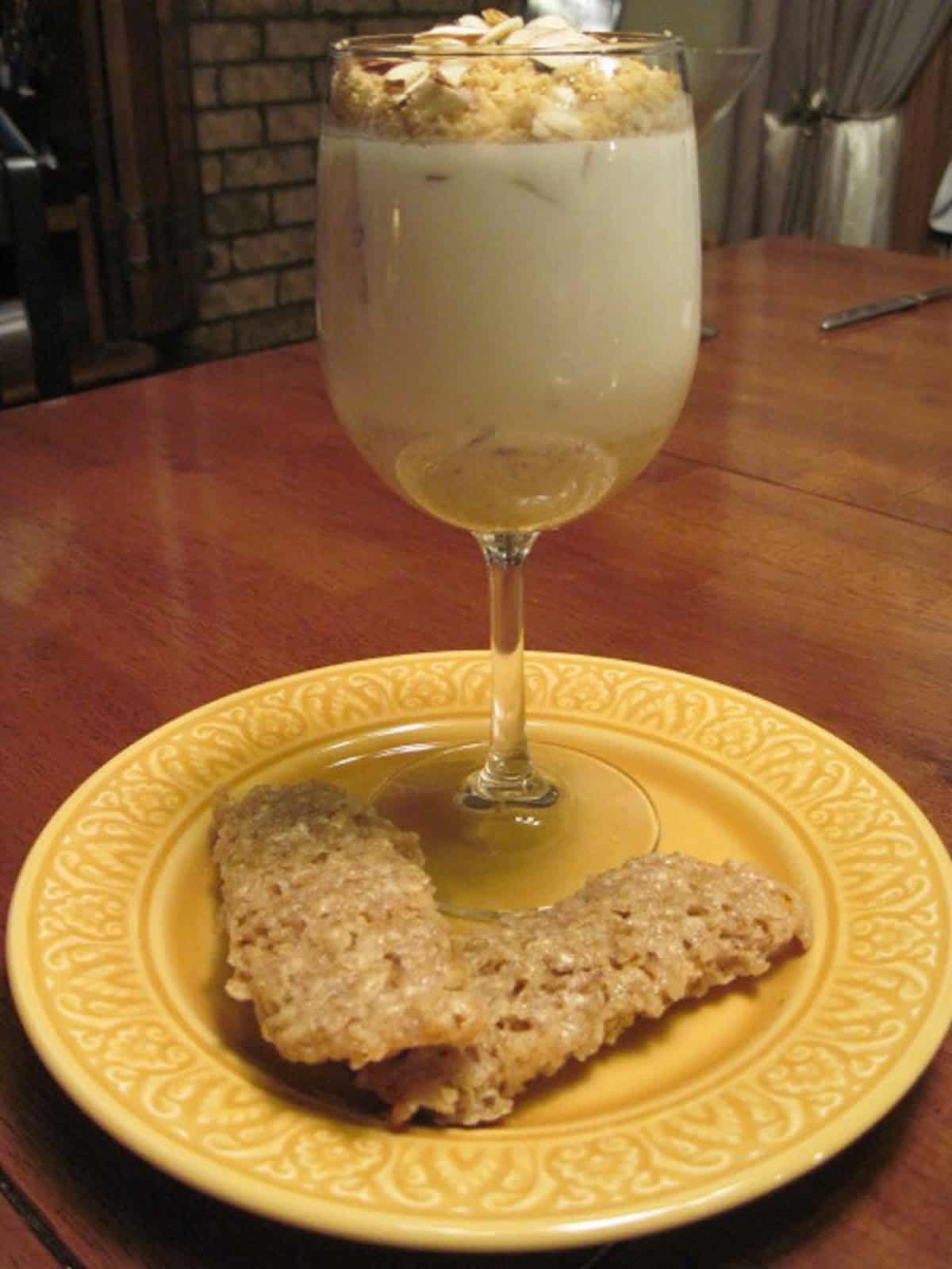 One wine glass on a yellow plate filled with Banana Panna Cotta with an almond and crumble topping.