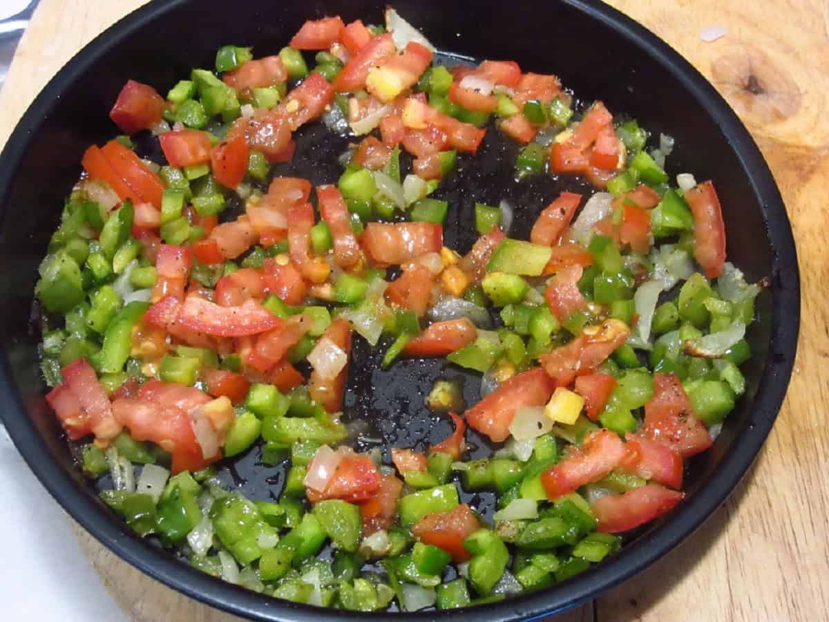 Cooked tomato, pepper, and onion in a round metal air fryer pan.