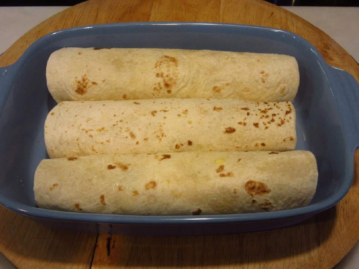 Wrapped air fryer breakfast burritos in a blue casserole dish.