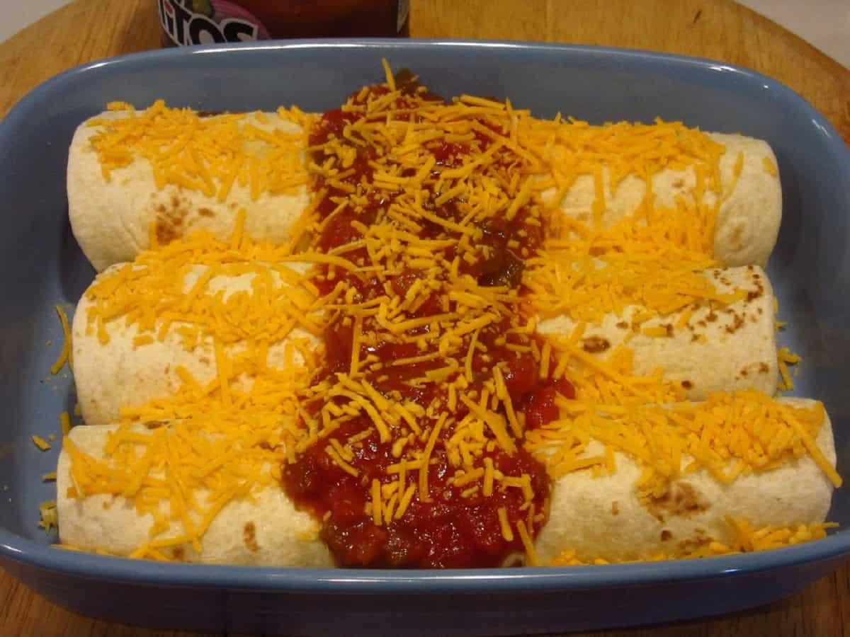 Three air fryer breakfast burritos topped with cheese and salsa in a blue casserole dish.