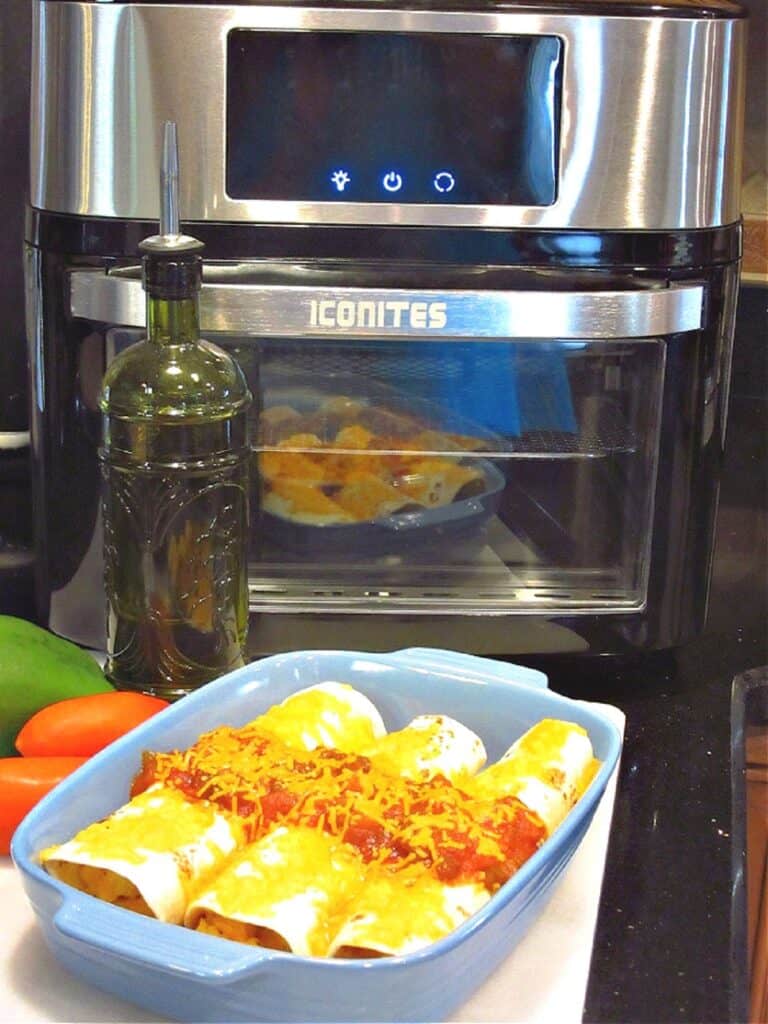 A blue casserole dish with three air fryer breakfast burritos in the foreground with an air fryer in the background.