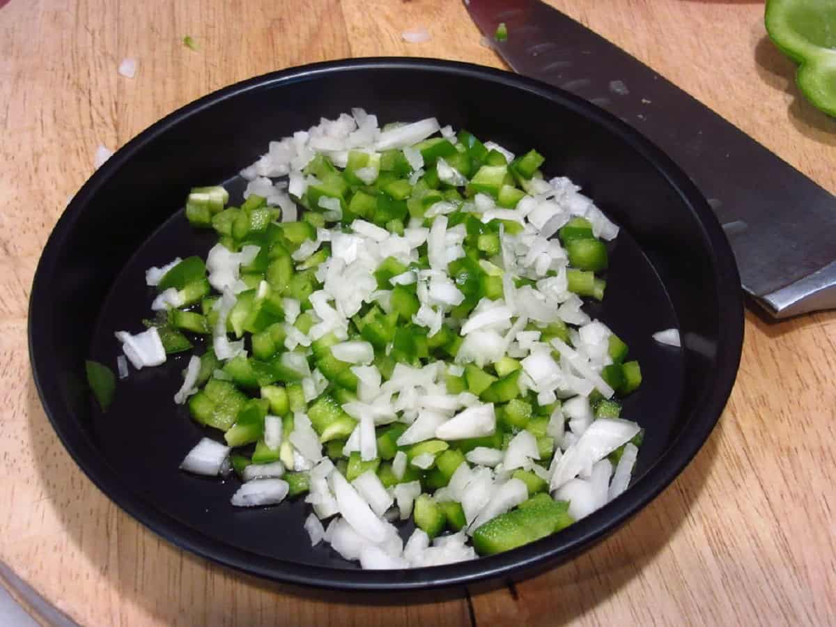 Diced green bell pepper and shallots in a metal air fryer pan.