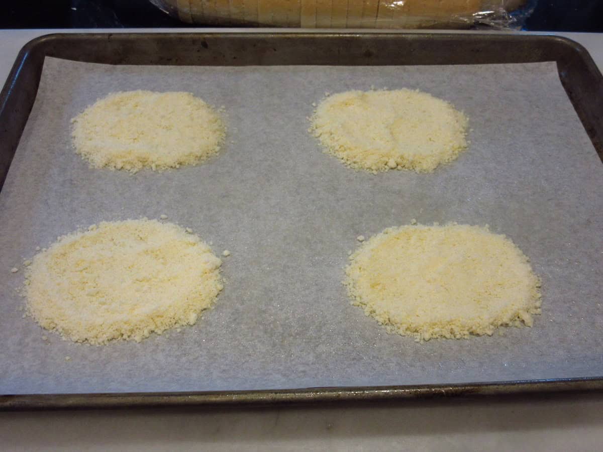 Four circles of grated Parmesan cheese on a baking sheet.