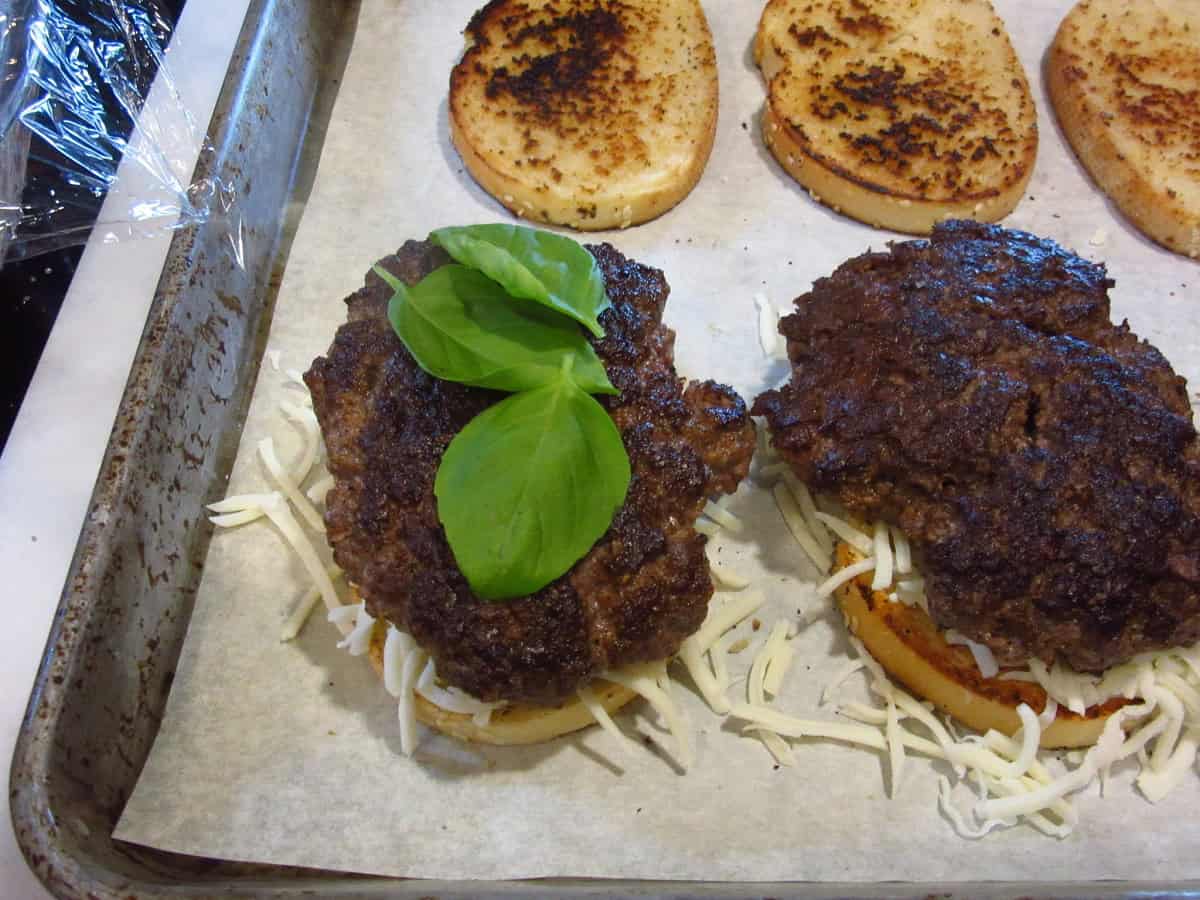 Burger patties on shredded mozzarella with basil leaves.