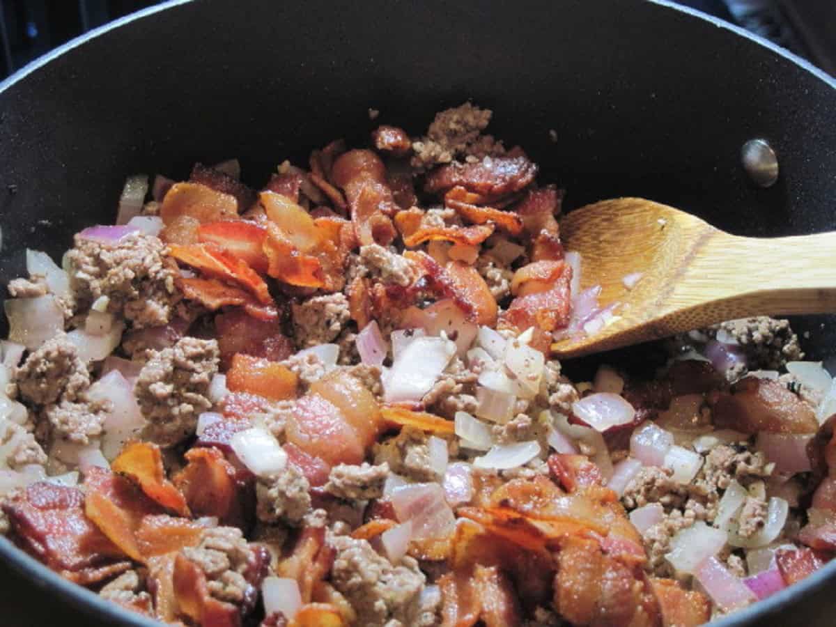 Cooked bacon, onion, and ground beef in a pot on the stove.