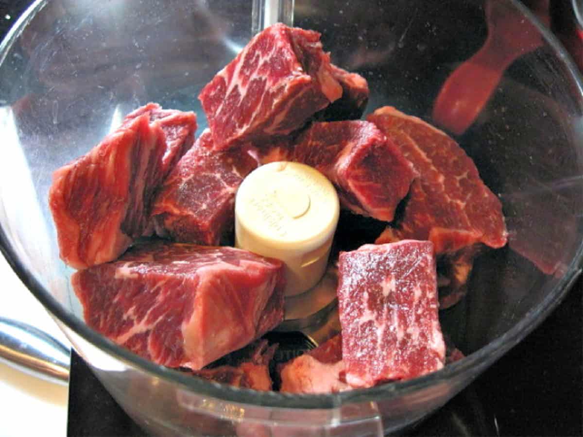 Pieces of boneless beef short ribs in a food processor.