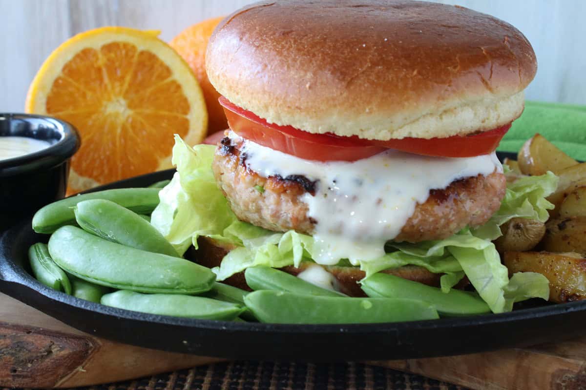 A delicious looking salmon patty on a bun with orange sauce, tomato, and lettuce.