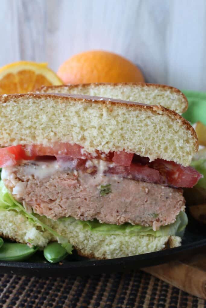A cut in half Salmon Burger with a bun and tomatoes.