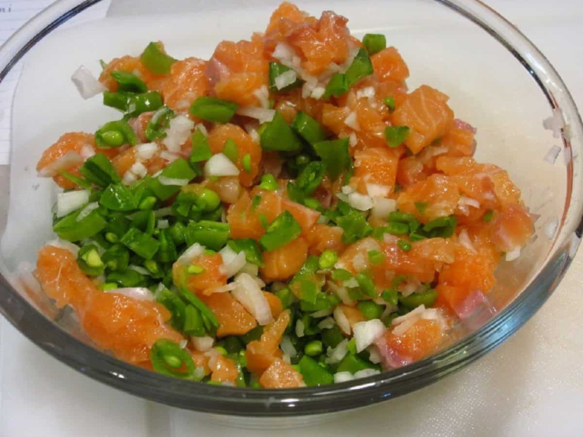 Diced salmon, shallots and peas in a glass bowl for making salmon burgers.