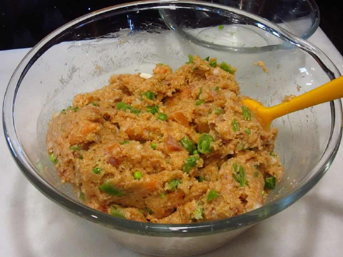 A mixture of ground salmon and scallions in a glass bowl with a spatula.