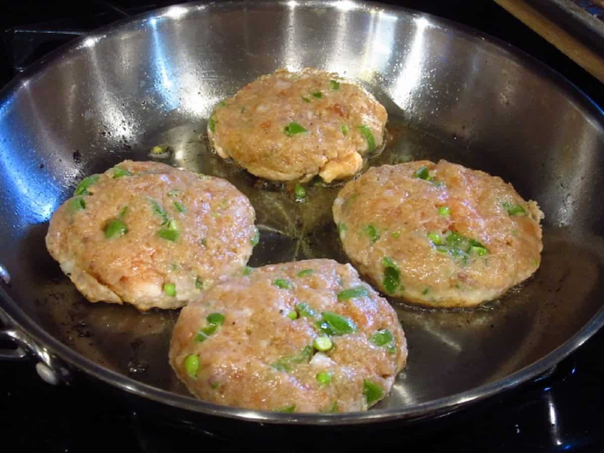 Four uncooked ground salmon patties in a skillet.