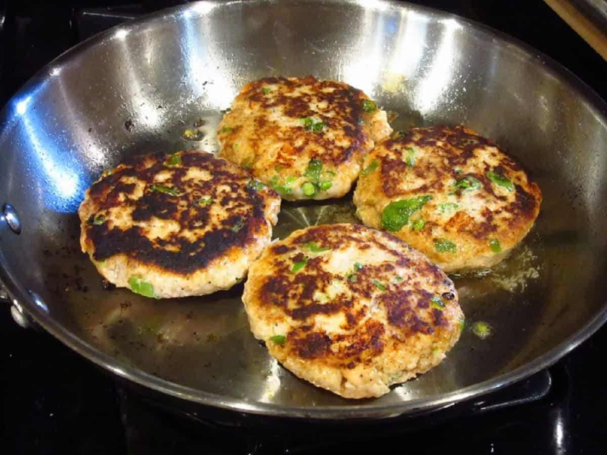 Four browned and cooked salmon patties in a large skillet.
