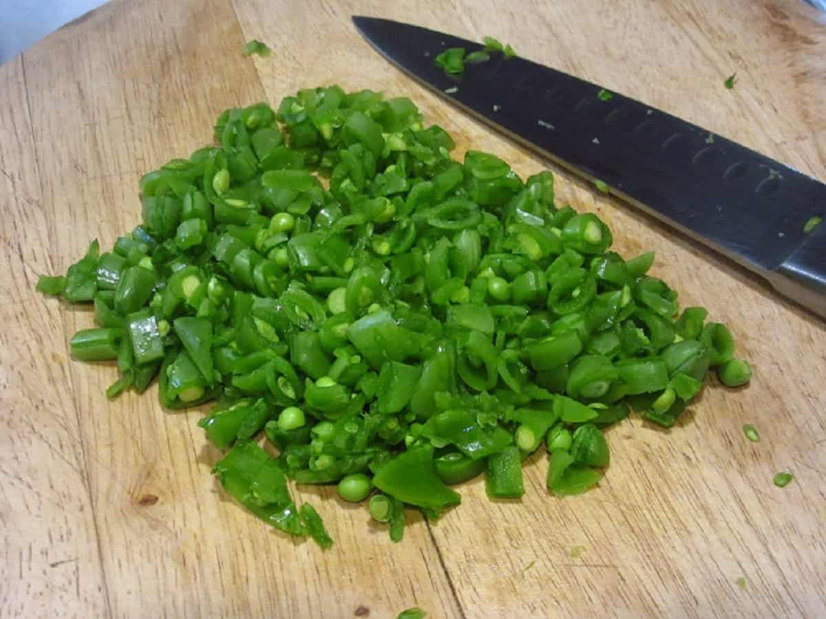 Chopped up sugar snap peas on a wooden cutting board.