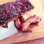 A wooden board with Slow Roasted Baby Back Ribs and a cleaver.