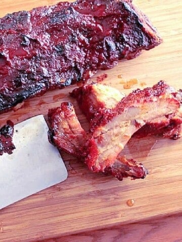A wooden board with Slow Roasted Baby Back Ribs and a cleaver.