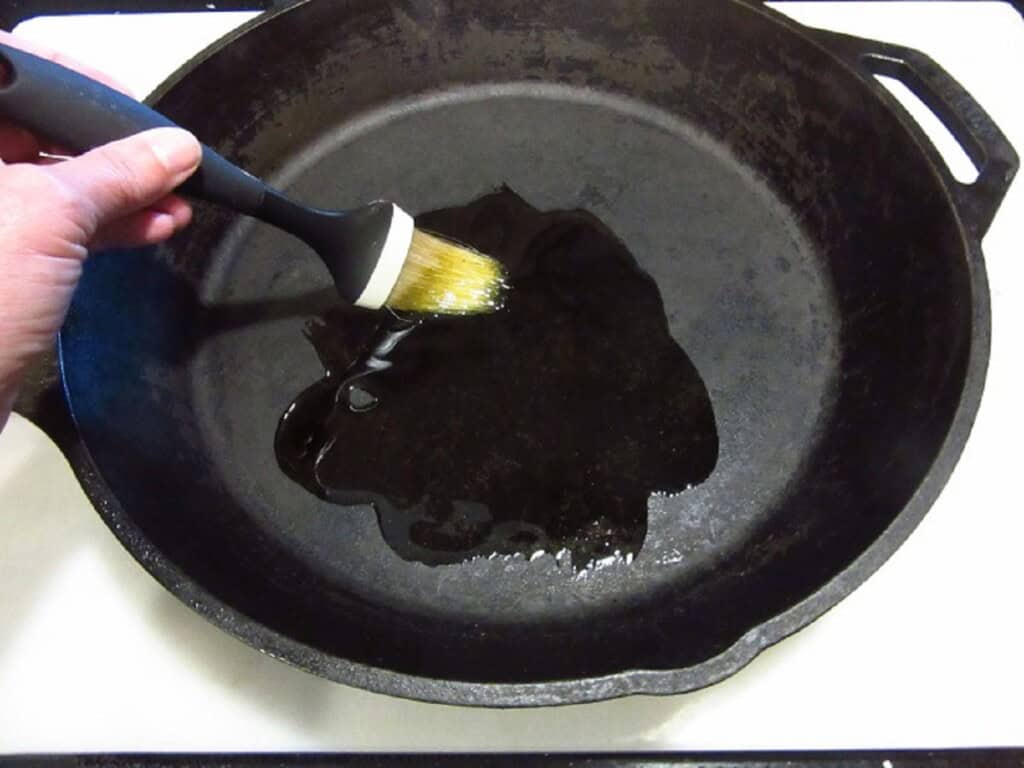Oil being brushed on the inside of a cast iron skillet.