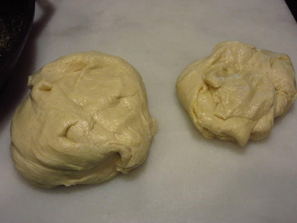 Two portions of pizza dough on a marble slab.