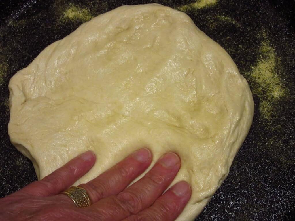 Fingertips pressing out a pizza dough inside a cast iron skillet.