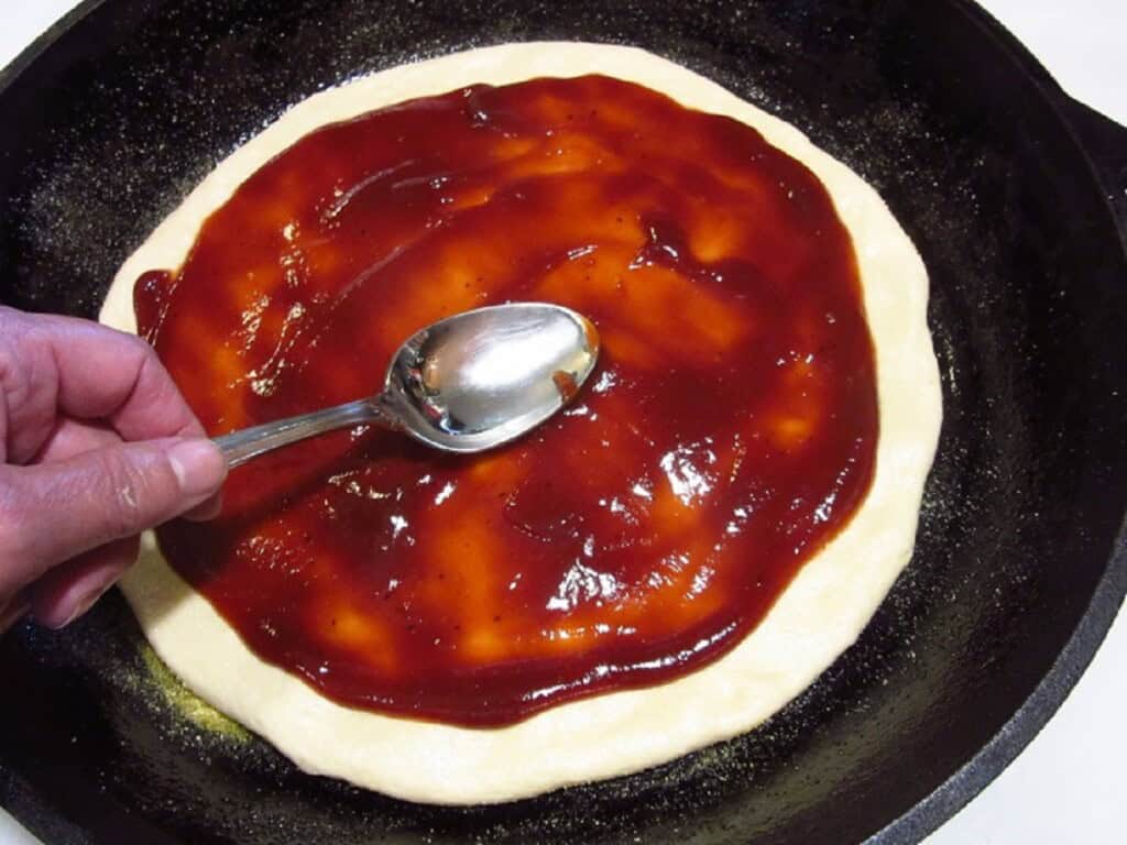 BBQ sauce being spread on an unbaked pie dough.
