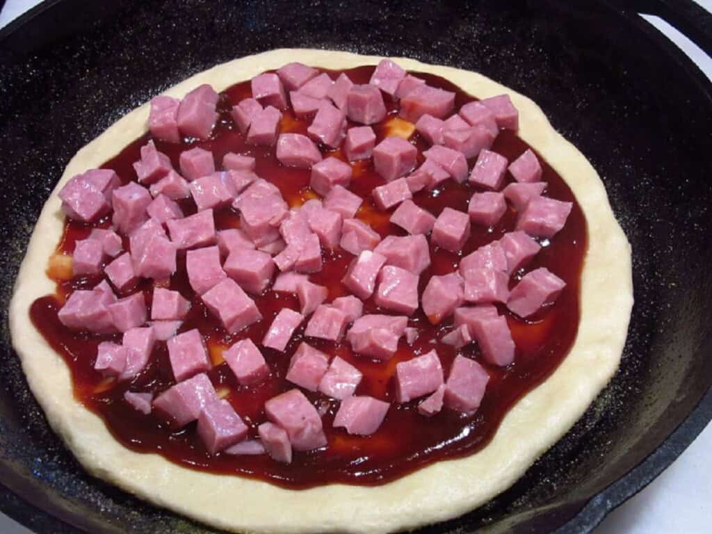 Chunks of ham on an unbaked pizza crust with BBQ sauce.