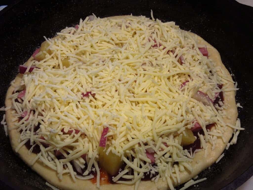 The toppings for a stuffed double crust Hawaiian pizza; mozzarella, onion, pineapple, and ham.