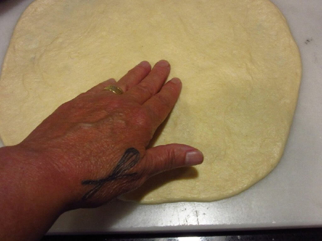 A hand pressing out a pizza pie crust.