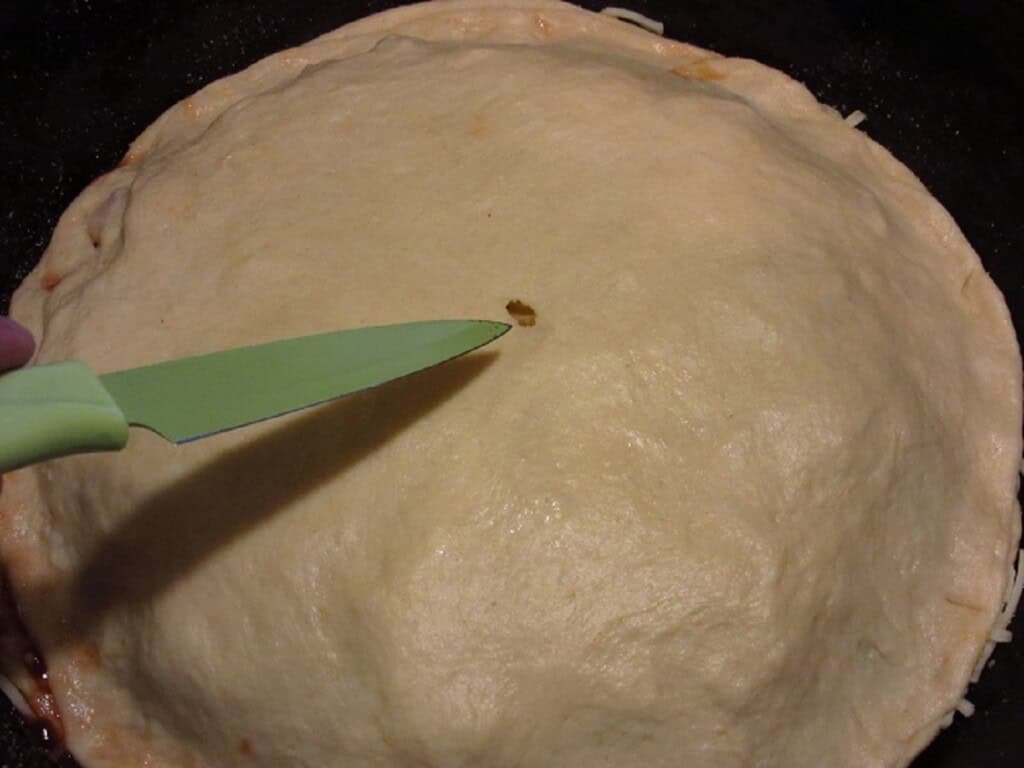 A hole on top of an unbaked pizza pie made with a pairing knife.