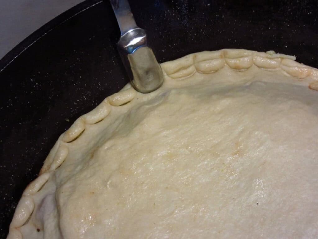 A measuring spoon making a scalloped edge on a stuffed double crust Hawaiian pizza.