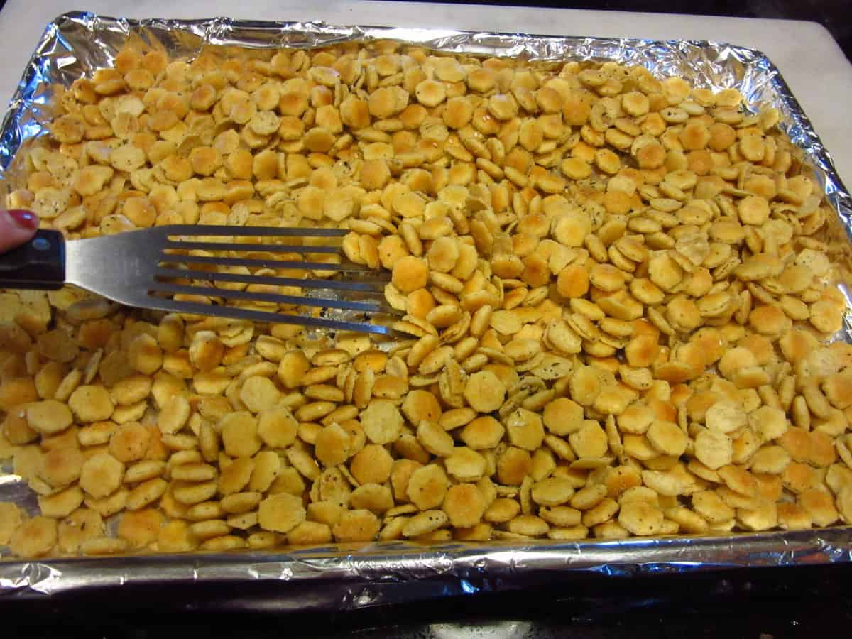 A spatula mixing oyster crackers on a baking sheet.