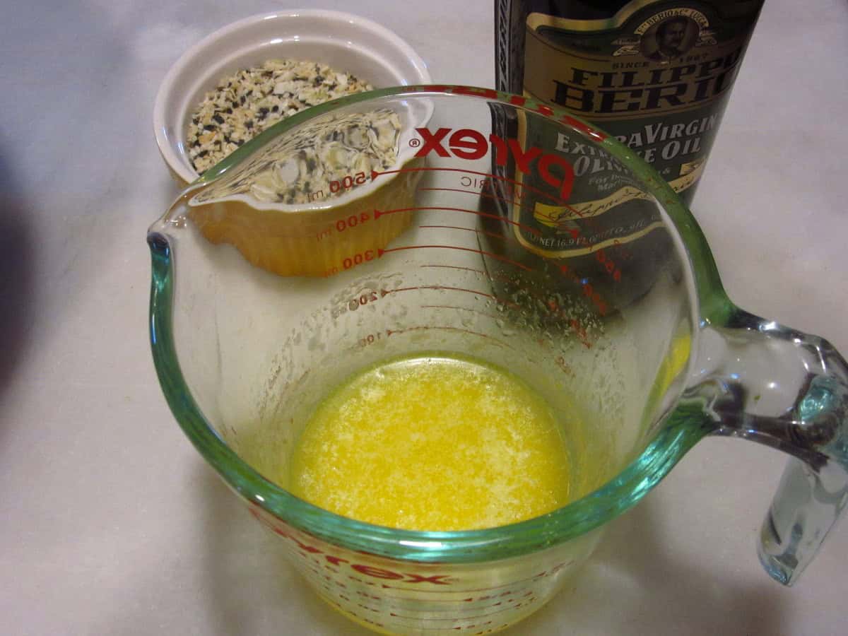 Melted butter in a glass measuring cup with olive oil and everything seasoning in the background.