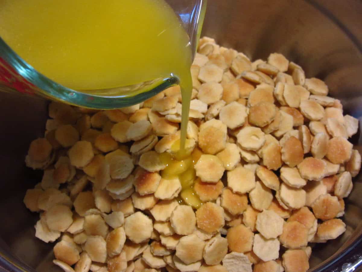Melted butter being poured into a large bowl with oyster crackers.