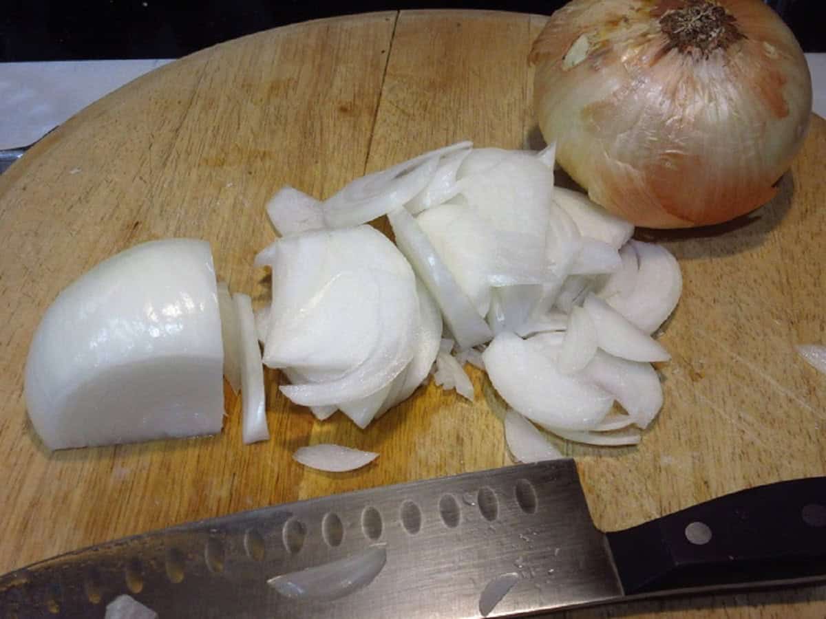 Sliced onions with a knife on a wooden cutting board.