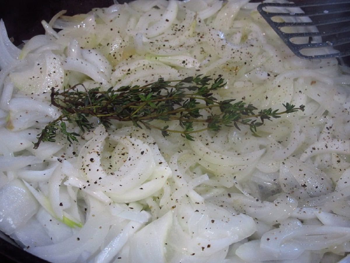 Fresh thyme sprigs in with sliced onions in a skillet.