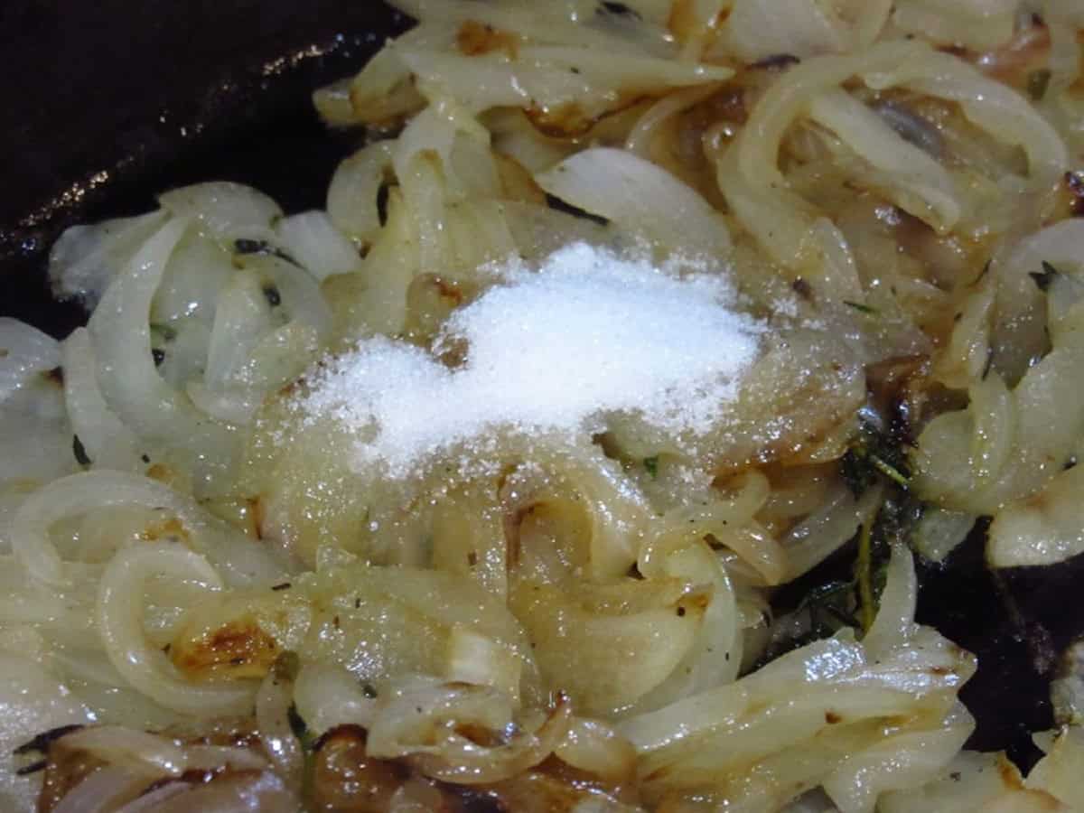 Sugar in a skillet with caramelized onion slices.