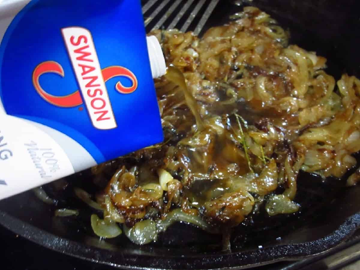 Beef stock being added to a skillet of caramelized onions.
