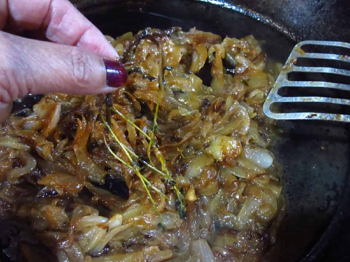 Removing a spent thyme sprig from a skillet of caramelized onions.