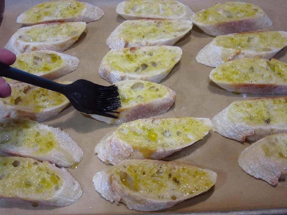 Olive oil being brushed on baguette slices.