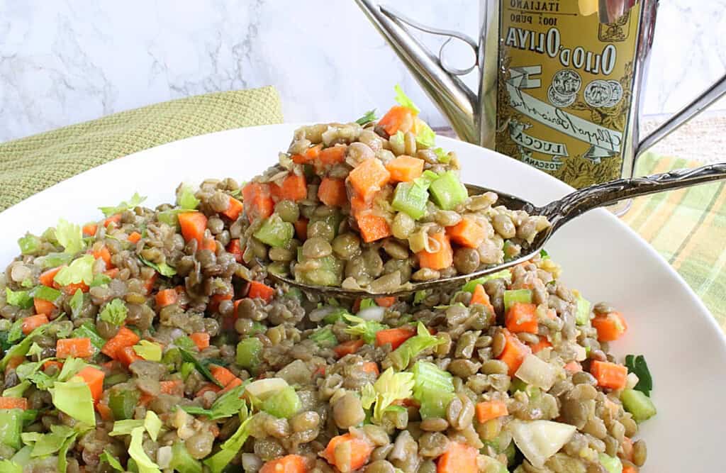 A serving spoon filled with French Lentil Salad over a white serving bowl.