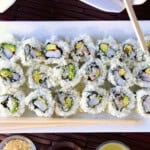 Avocado Shrimp Sushi Rolls on a white plate with chopsticks and rice.